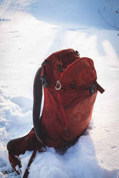Small red backpack stands on the white snow