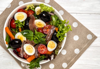 Top view. French cuisine. Traditional niçoise (nicoise) salad in a white plate on a polka dot napkin. White background.