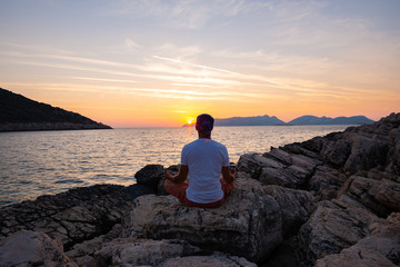 Traveler sits on the rock seashore and practicing yoga