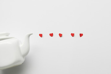 top view of tea pot and red paper cut hearts on white background