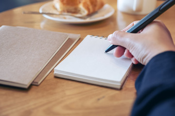 Closeup image of a hand writing on blank notebook on wooden table