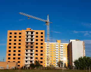Fototapeta na wymiar Construction of new apartment building. Facade of unfinished brick multistory building with crane and new dwelling on the background