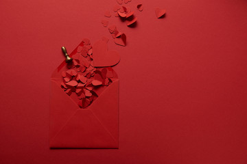 top view of paper cut hearts and opened envelope on red background