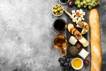 Obraz na płótnie Canvas Snacks with wine - various types of cheeses, figs, nuts, honey, grapes, bread on a gray background. Top view, copy space. Food background