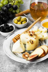 Snacks with wine - various types of cheeses, figs, nuts, honey, grapes on a gray background