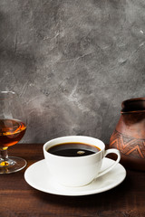 Coffee in white cup with cognac and clay cezve on wooden background. Copy space. Food background