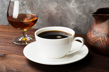 Coffee in white cup with cognac and clay cezve on wooden background