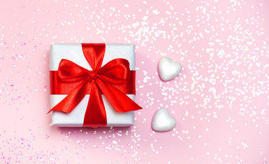 gift box vith red bow and glitter sparkles and confetti on pink background. st. Valentine's day concept.