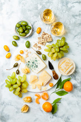 Cheese platter with different cheeses, grapes, nuts, honey. Appetizers table with antipasti snacks. Cheese variety board over white marble background. Top view, flat lay