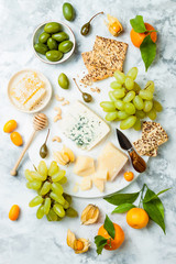 Cheese platter with different cheeses, grapes, nuts, honey. Appetizers table with antipasti snacks. Cheese variety board over white marble background. Top view, flat lay