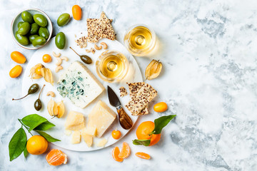 Cheese platter with different cheeses, grapes, nuts, honey. Appetizers table with antipasti snacks. Cheese variety board over white marble background. Top view, flat lay