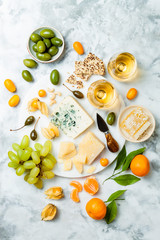 Cheese platter with different cheeses, grapes, nuts, honey. Appetizers table with antipasti snacks. Cheese variety board over white marble background. Top view, flat lay