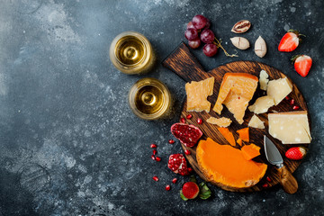 Cheese variety board or platter with cheese assortment, grapes, honey, nuts and wine in glasses. Black stone background. Top view, flat lay