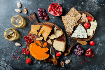 Cheese variety board or platter with cheese assortment, grapes, honey, nuts and wine in glasses. Black stone background. Top view, flat lay