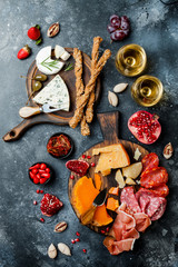 Obraz na płótnie Canvas Appetizers table with italian antipasti snacks and wine in glasses. Brushetta or authentic traditional spanish tapas set, cheese variety board over black stone background. Top view, flat lay