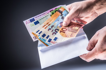 Male hand inserted into the envelope euro banknotes - bribe and corruption concept.