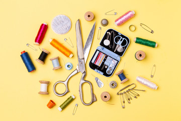 Composition with threads and sewing accessories - scissors, centimeter, pins on yellow background.