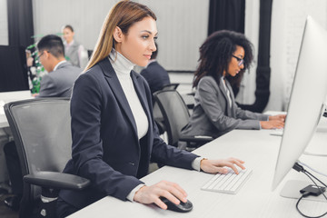 side view of focused young businesswoman using desktop computer at workplace