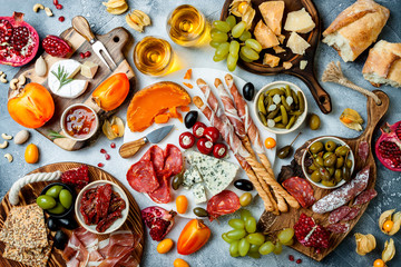 Fototapeta na wymiar Appetizers table with antipasti snacks and wine in glasses. Authentic traditional spanish tapas set, cheese and meat platter over grey concrete background. Top view