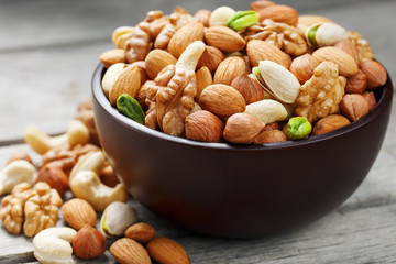 Wooden bowl with mixed nuts on a wooden gray background. Walnut, pistachios, almonds, hazelnuts and cashews, walnut.