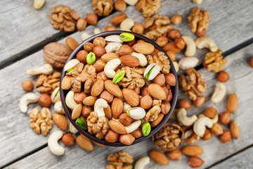 Wooden bowl with mixed nuts on a wooden gray background. Walnut, pistachios, almonds, hazelnuts and cashews, walnut.