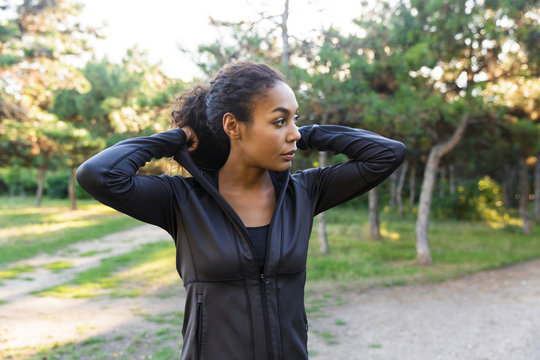 Image of adorable woman 20s wearing black tracksuit, walking through green park