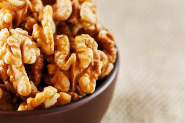 Peeled walnuts in a wooden, dark brown cup on a burlap cloth.
