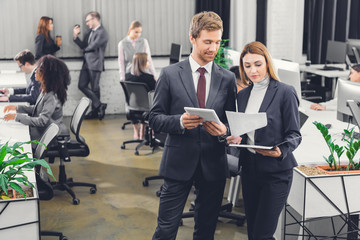 professional young businessman and businesswoman discussing papers while standing together in open space office
