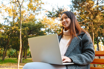 Smiling young asian woman wearing coat sitting on a bench