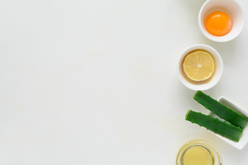 Fresh ingredients for homemade effective acne remedies on white background. Honey, sea salt, egg yolk, olive oil, oat, lemon and aloe. Flat lay. Copy space