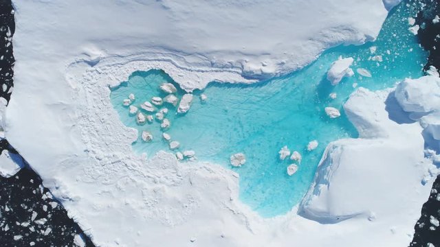 Antarcic Iceberg Turquoise Melt Hole Aerial View. Ecological symbol: Melting Ice. Nature Lake with Blue Water in Floating Ocean Ice Piece. Climate Change Global Warming Concept Top Zooming Out Drone
