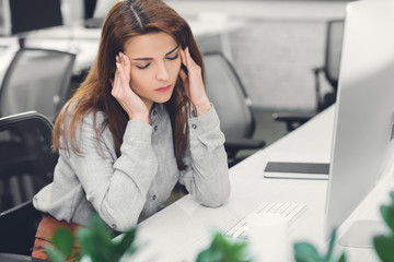 young businesswoman with closed eyes suffering from headache at workplace