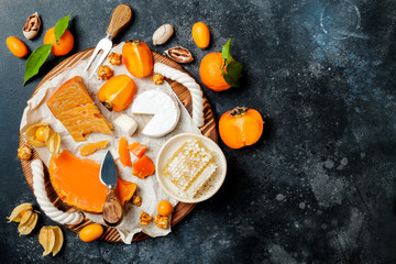 Fototapeta na wymiar Cheese variety board or platter with cheese assortment, persimmons, honey and nuts. Black stone background. Top view, flat lay