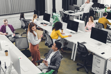 high angle view of young multiracial coworkers working and talking in open space office