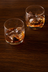 Two glasses of whiskey with ice on a wooden background