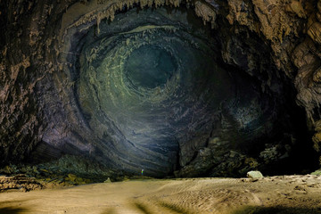 Man with headlight standing on a rock under a high wall with stalactites inside the giant Hang Tien cave in the Phong Nha Ke national park in Vietnam.