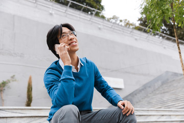 Obraz premium Smiling young asian man talking on mobile phone