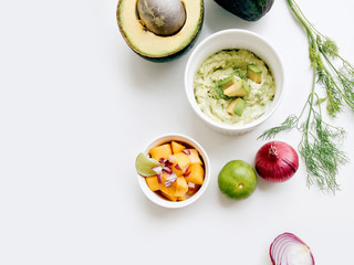 Healthy creamy avocado dip and mango salsa with fresh ingredients on a white background, top view with copy space