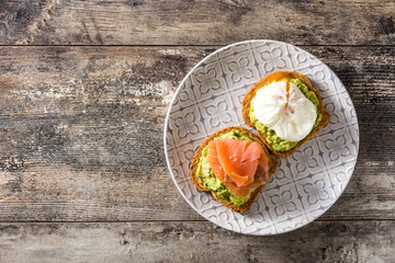 Toasted breads with poached eggs, avocado and salmon in plate on wooden table. Top view. Copyspace