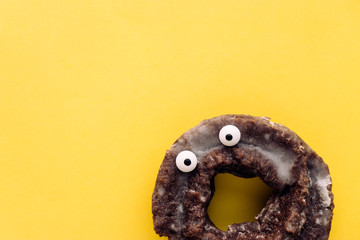 Funny shock face glazed chocolate cake donut on a pastel yellow background, creative minimal Halloween concept with copy space