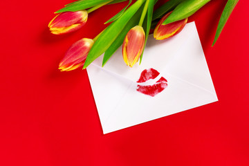 Valentine's day background. Love letter concept. White envelope with red lipstick kiss and bouquet of tulips on red.