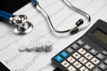 Stethoscope, pills and calculator are on a sheet with an electrocardiogram