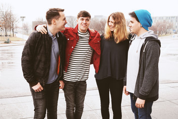 group of four young urban teenage friends having fun and laughing together despite bad weather - candid real people