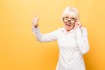 I'm winner! Portrait of a cheerful senior woman gesturing victory isolated over yellow background....