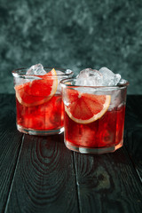 Delicious close up view on red fresh alcoholic cocktail from cranberries. Glass with ice, beverage, grapefruit and bar utensils on dark wooden background. Copy free space for your text, logo or brand.