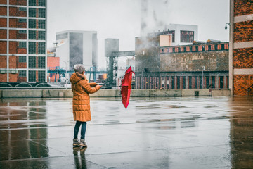 Woman with red umbrella is walking in idustrial city during blizzard