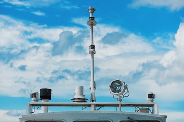 Marine navigation equipment. Communication mast of modern yacht with set of antennas, navigation lights, signal horn. Close-up of roof of ship is isolated on blue sky with clouds.
