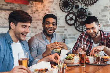 Three men enjoying burgers and beer in bar