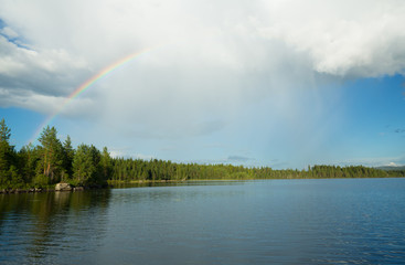 Rainbow over a swedish lake a summers day, rain is falling from the clouds. 