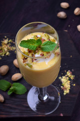 Mango yogurt dessert in a champagne glass topped with pistachios and mint against the dark background